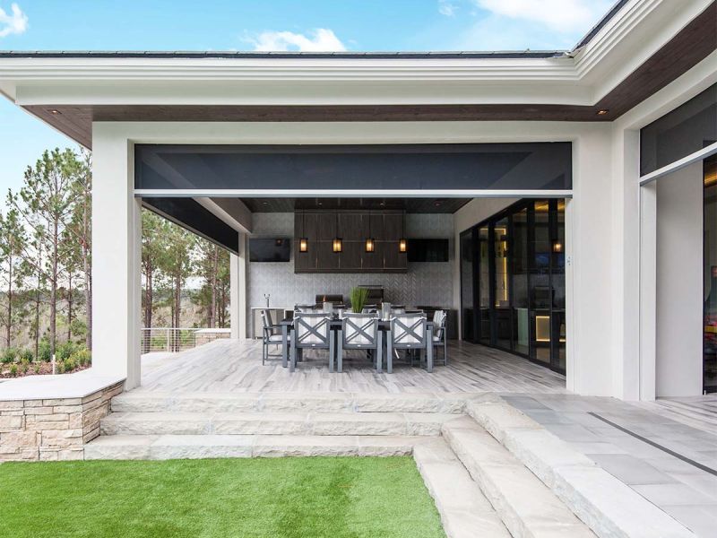 Modern outdoor dining pavilion with motorized Phantom screens lowered across wide openings, revealing forest view beyond.