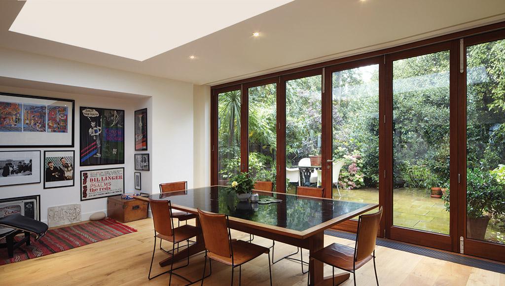 Bright dining room with a large wooden table and framed wall art, featuring expansive glass patio doors that look out onto a lush, green garden courtyard.