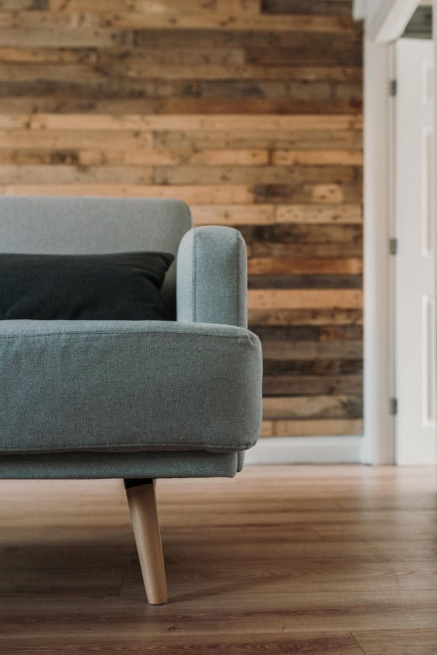 Close-up of a modern gray sofa leg on hardwood flooring with a reclaimed wood accent wall in the background.