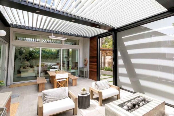 Covered patio with a motorized louvered pergola, outdoor seating, and a modern fire feature.